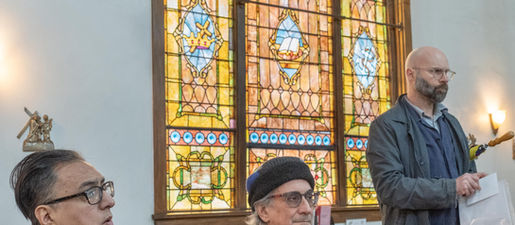 Three men sit in front of a stained glass window.