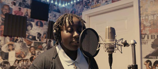 A teenager wearing headphones sings into a microphone.