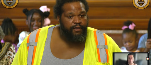A Black man with a beard wears a safety vest. An American Sign Language interpreter appears in a box at lower right. Behind the man, young Black girls with bows in their hair sit on polished wooden benches.