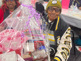 Two older, brown-skinned women hold a large gift basket between them.