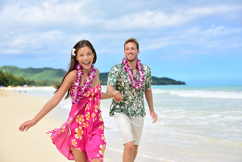 Happy couple having fun running on Hawaii beach vacations in Hawaiian clothing wearing Alo