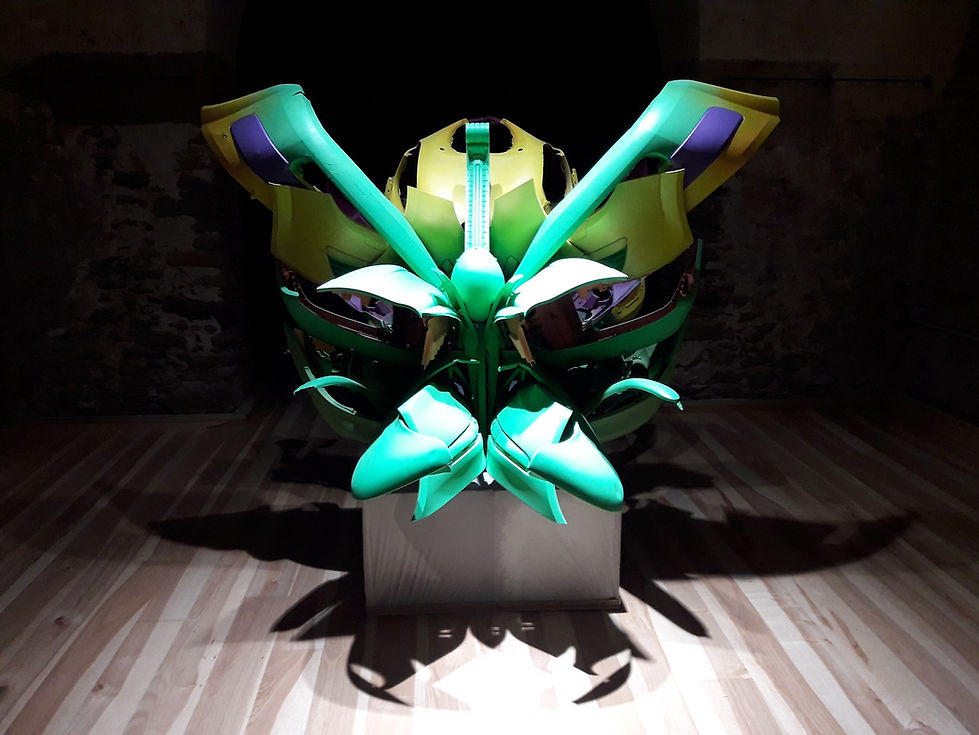abstract sculpture by artist Natalie Mandel, made from plastic car parts and placed in a gallery with dramatic light.