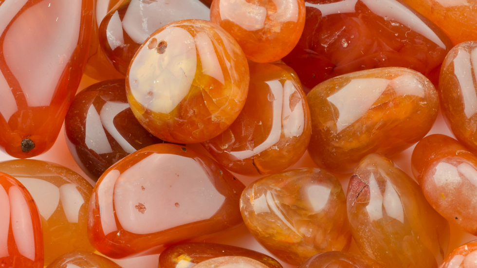Smooth, polished orange and red stones with glossy surfaces, closely packed together. No text or background visible. Warm and vibrant mood.