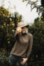 Woman smiles holding yellow flower toward camera in cozy fall outfit, brown turtleneck tunic sweater, olive green skinny cargo pants, ankle booties, wide brim hat, fashion blog, casual fall outfit ideas