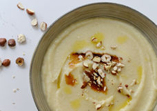 Creamy cauliflower and parsnip soup in a bowl, topped with hazelnuts and a drizzle of olive oil