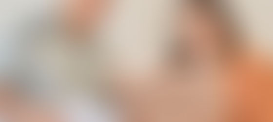 In an office-like setting, a woman holding a laptop and pointing at the screen speaks with a man who looks on attentively while holding papers.