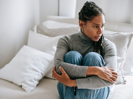 Woman sitting in a bed looking distraught, holding her legs to her chest