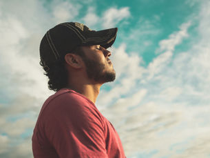 Man with beard wearing a black cap with closed eyes facing the sky