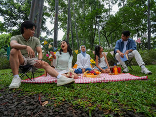 Group of five young people laughing, eating, and having a picnic in the park