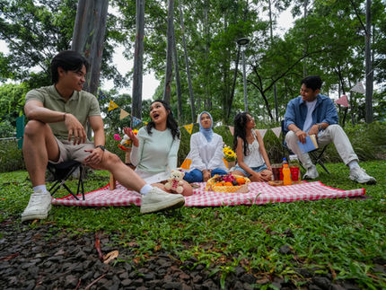 Group of five young people laughing, eating, and having a picnic in the park