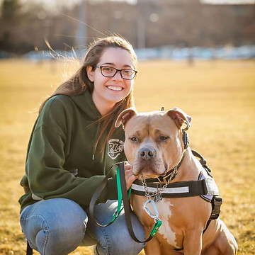 Image of Michelle (head trainer) posing next to her fawn American Bully, Taz . There is a field behind them.