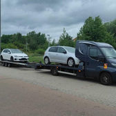 Ciemna laweta transportująca dwa białe VW Golfy na parkingu.
