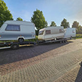 Trzy używane przyczepy kempingowe transportowane na lawetach po brukowanej drodze.