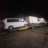 Biała laweta transportująca furgonetki i busa nocą na drodze.