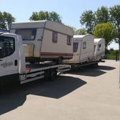 Biała laweta transportująca wiele przyczep kempingowych na słonecznym parkingu zewnętrznym.