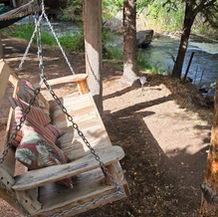 Wooden swing beside the creek at Cedaredge Lodge surrounded by trees and nature