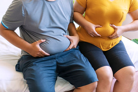 Man and woman holding their big belly while sitting on the bed