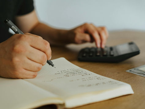 A person sitting at a desk using a calculator and taking notes in a notebook