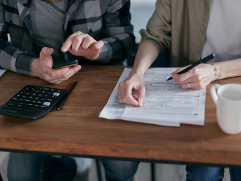 two people sitting at a desk reviewing a stack of paperwork