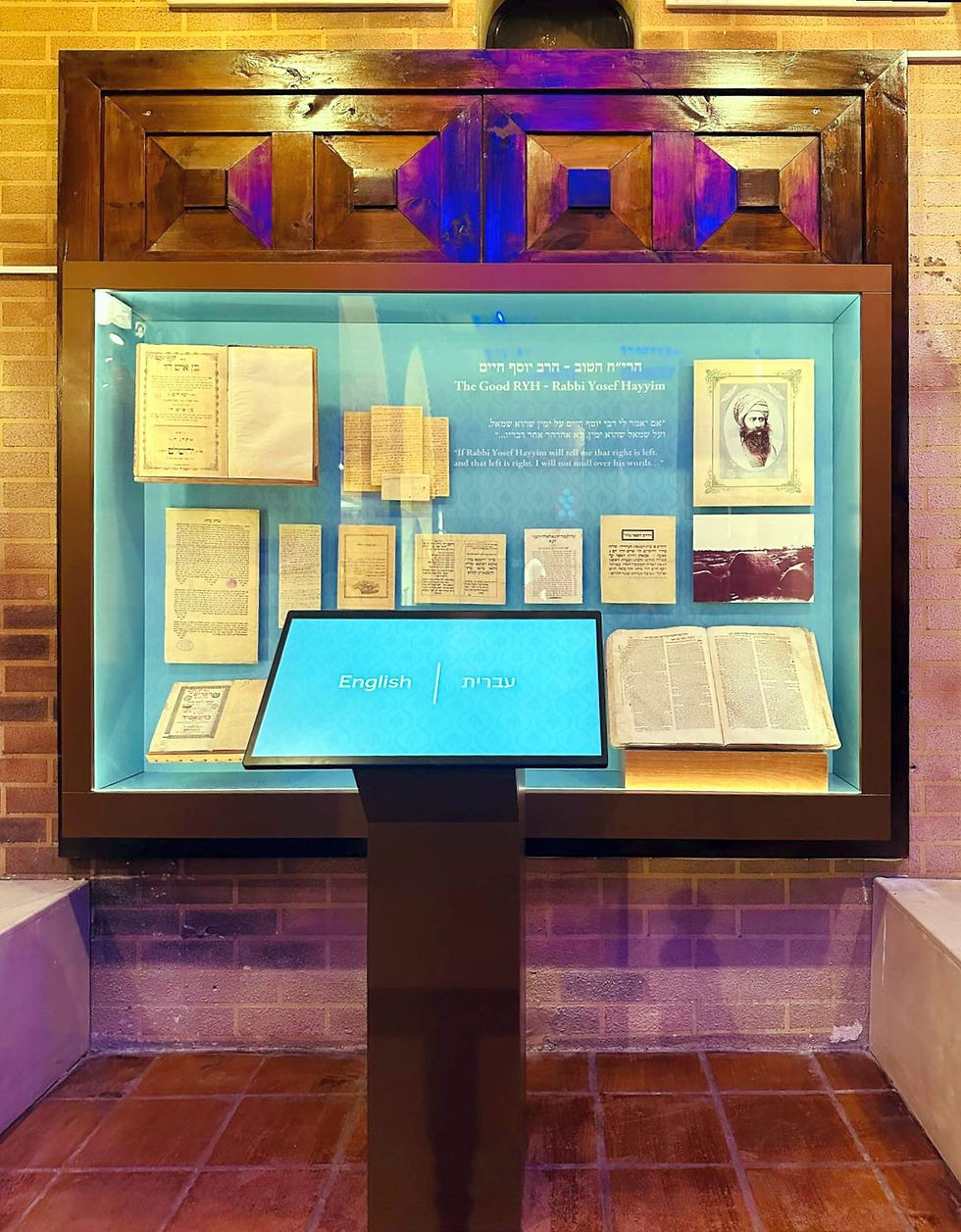 Display of Rabbi Yosef Hayyim's works in a wooden-framed exhibit. Includes old texts and a portrait. Interactive screen offers English and Hebrew.