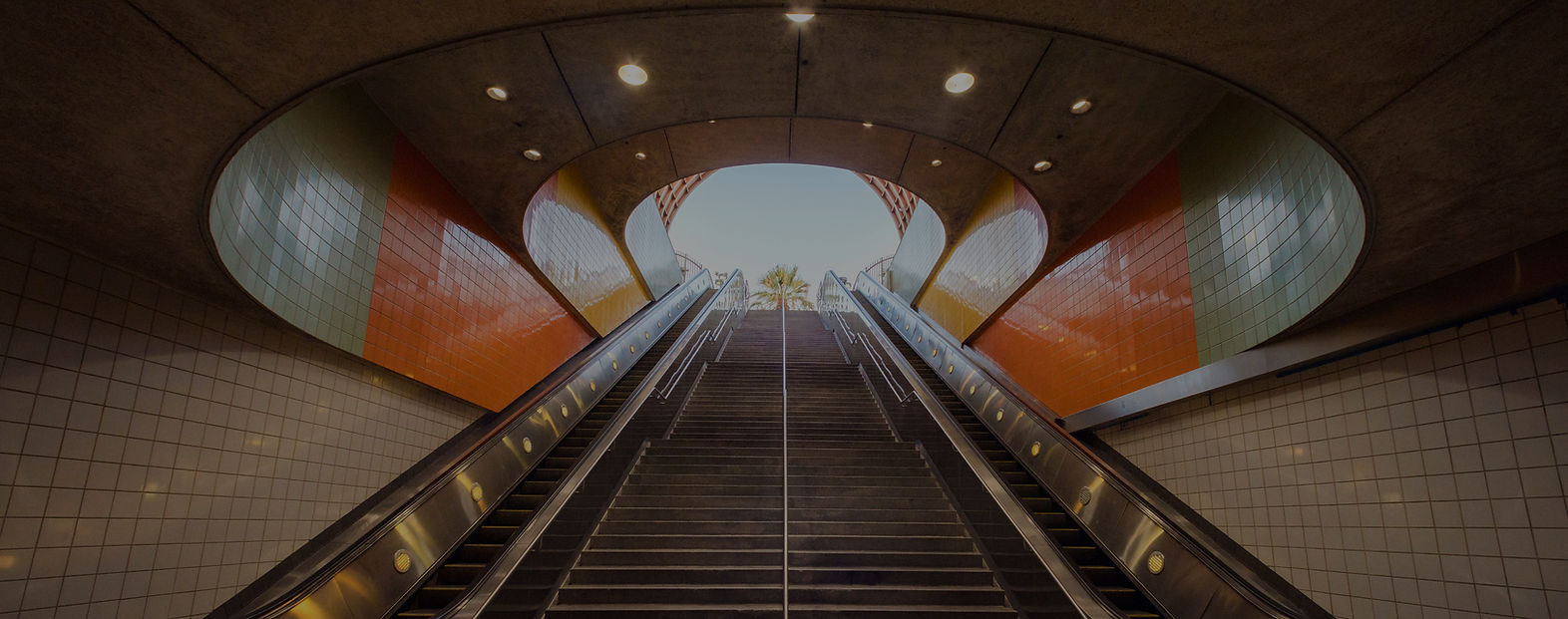 Long escalator ascending into a bright arched tunnel