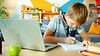 happy child using laptop for education writing in notebook doing homework sitting at desk