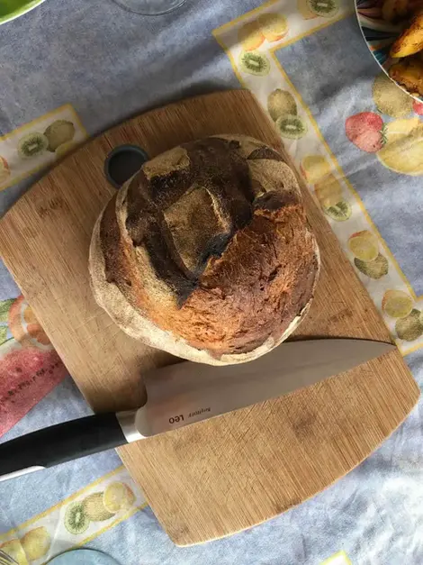 Pain rond artisanal croustillant sur planche en bois avec couteau.