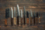 Various kitchen knives are arranged neatly on a rustic wooden table, showcasing different