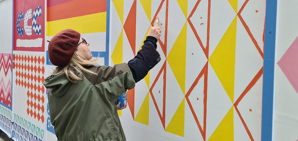 A woman painting a orange triangle onto a building site hoarding.