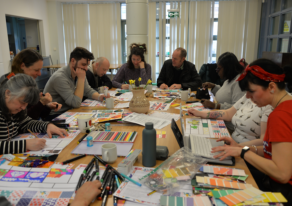 A group of people engaged in a colourful art workshop around a table with paper, pens, and pattern sheets. Bright, creative atmosphere.