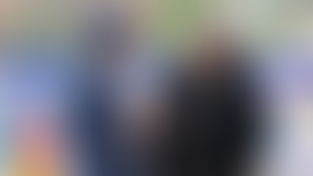 Rose, founder of CCC, and another woman talking and smiling in front of a colourful mural. One wears a blue coat and beanie, the other a black fur coat. Urban setting.