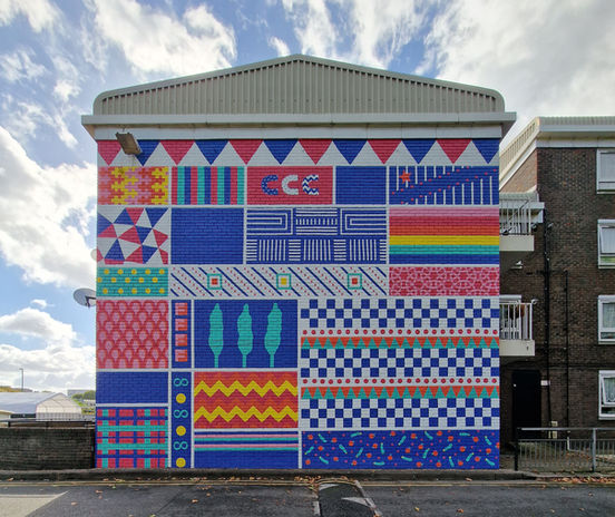 This is a Vibrant 1-meter high by 9-meter wide patterned mural co-designed with Co-Creative Connection Community Mural on the Teviot Estate building in partnership with the Hill Group and Poplar HARCA, 2022.