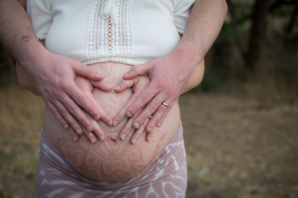 Pregnant belly adorned with henna, embraced by both parents’ hands, representing connection, support, and prenatal bonding.