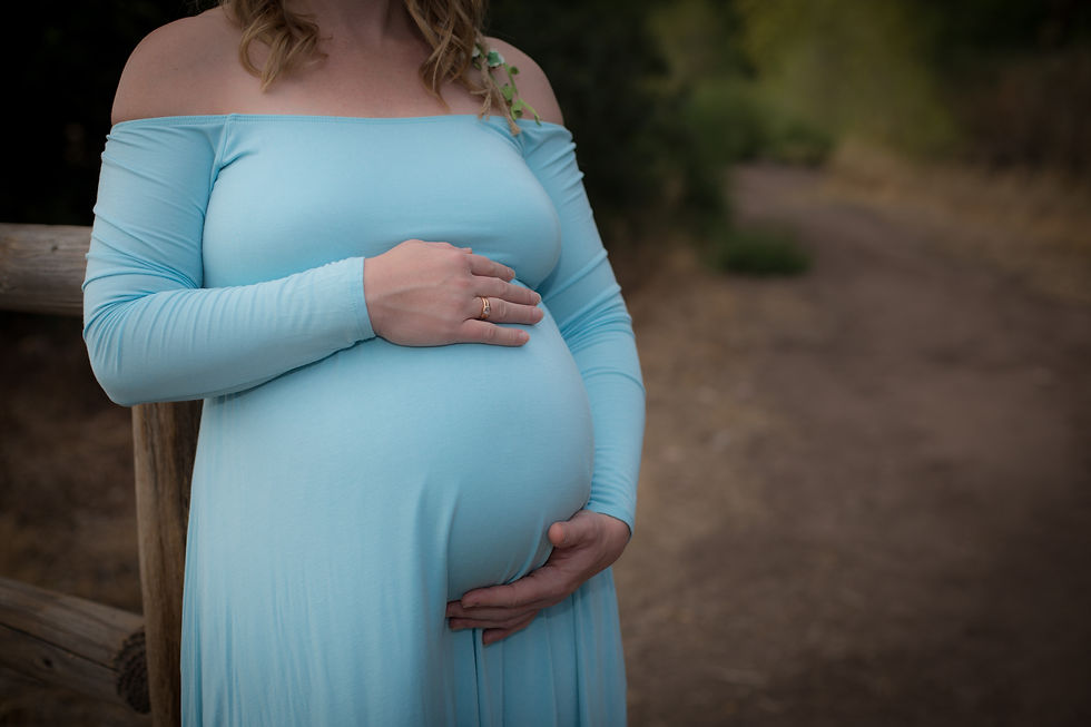 Pregnant woman in blue dress holding her belly during maternity photo shoot, symbolizing prenatal wellness and motherhood.