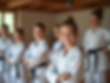 A group of smiling children and adults in a dojo, some practicing stances, others being gu