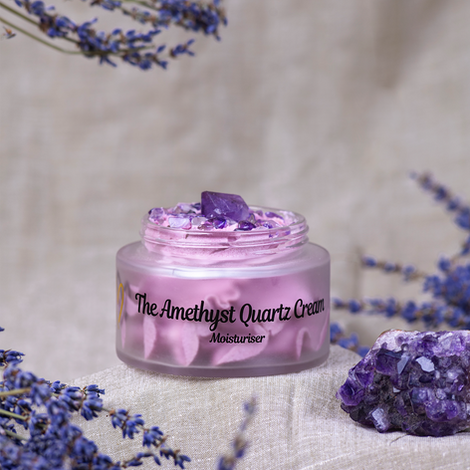 A jar of Zoe Bee’s Amethyst Quartz Cream, surrounded by lavender flowers and amethyst crystals, with a smooth swirl of lilac cream topped with gemstone pieces.