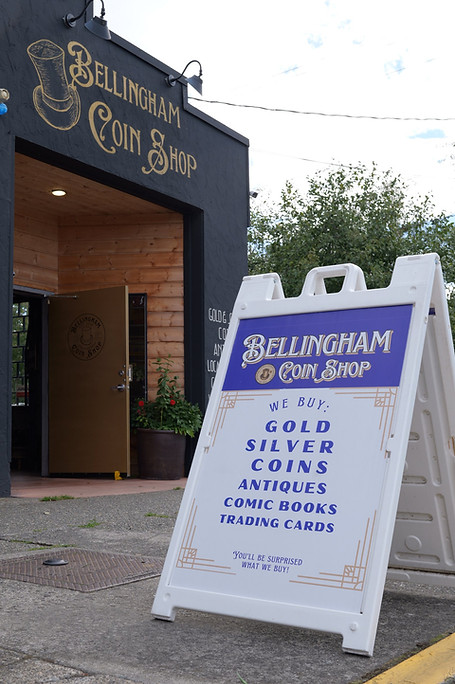 The front door of the Bellingham Coin Shop on a sunny day with a sign out front.