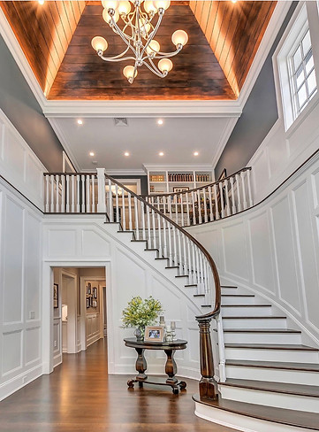 Elegant curved staircase with gray walls, crisp white trim detailing, and a rich mahogany-stained handrail, showcasing sophis