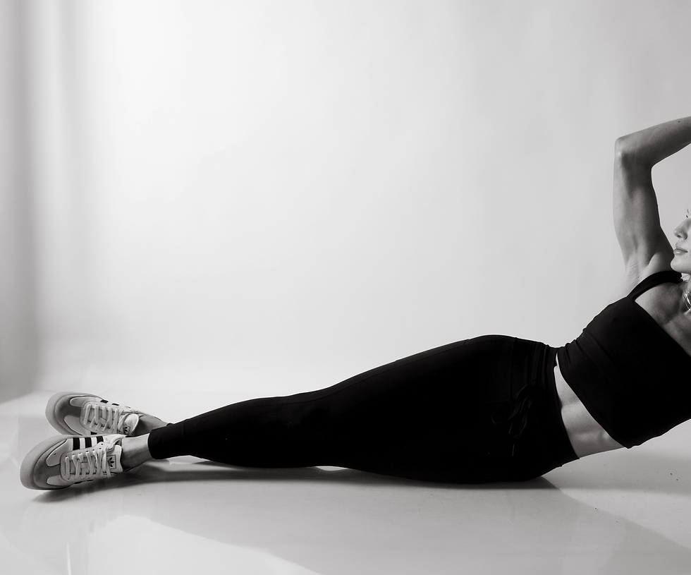 Woman in workout attire, performing side crunches on a smooth, light background. Wearing black top and leggings, striped shoes, focused.