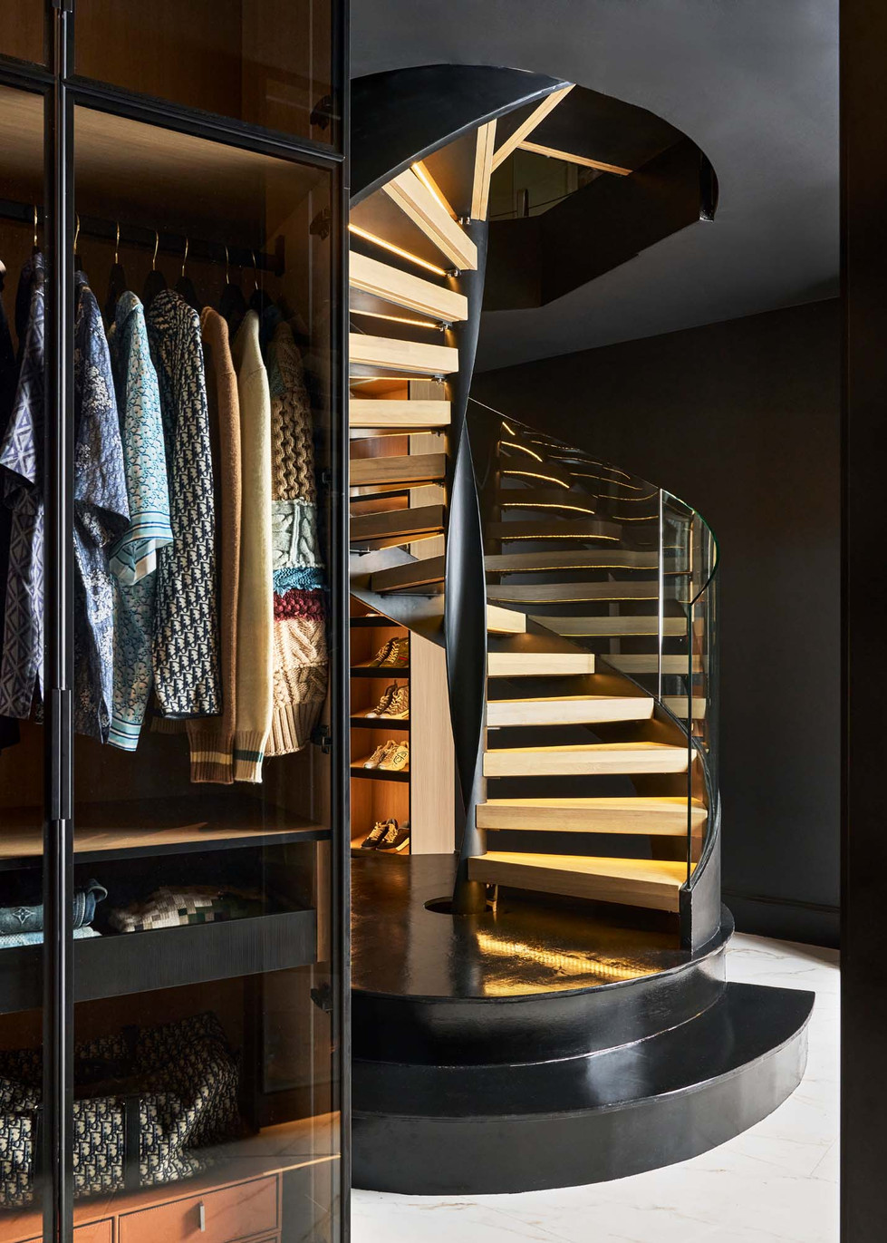 Black spiral staircase with lighted wood treads connecting two walk-in closets