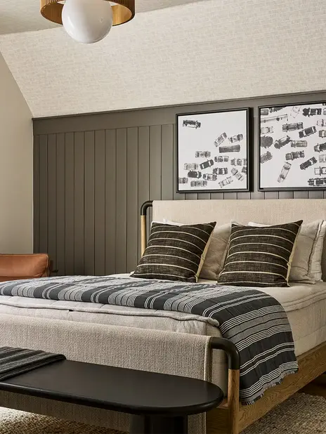 Boys bedroom with dark paneled wall, upholstered bed, leather chair, black nightstand, modern lighting, and neutral bedding