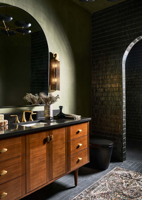 Walnut bathroom vanity with brass faucet, arched mirror, and green tile walls