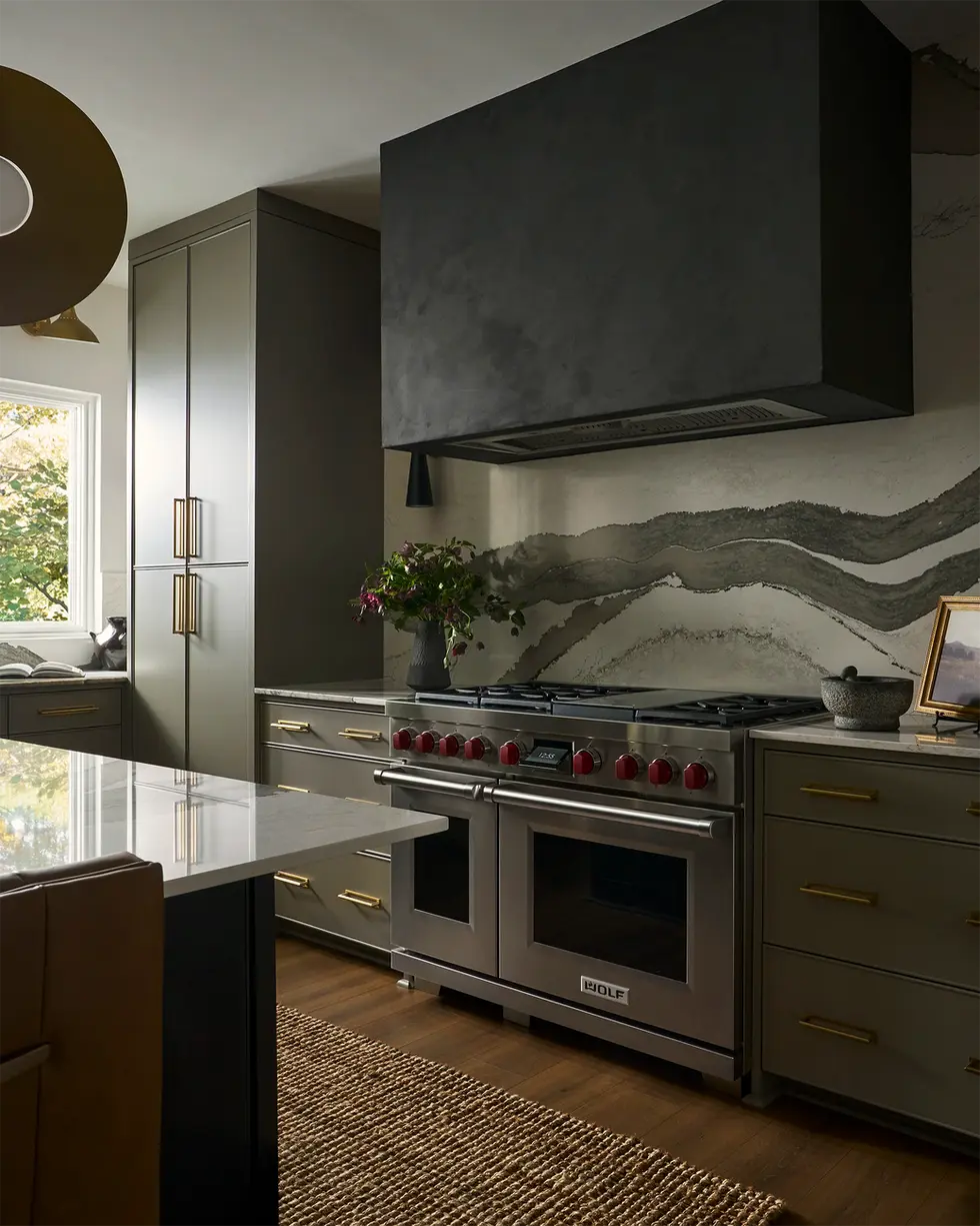 Gas range with black sculptural hood and dramatic stone slab backsplash in modern kitchen