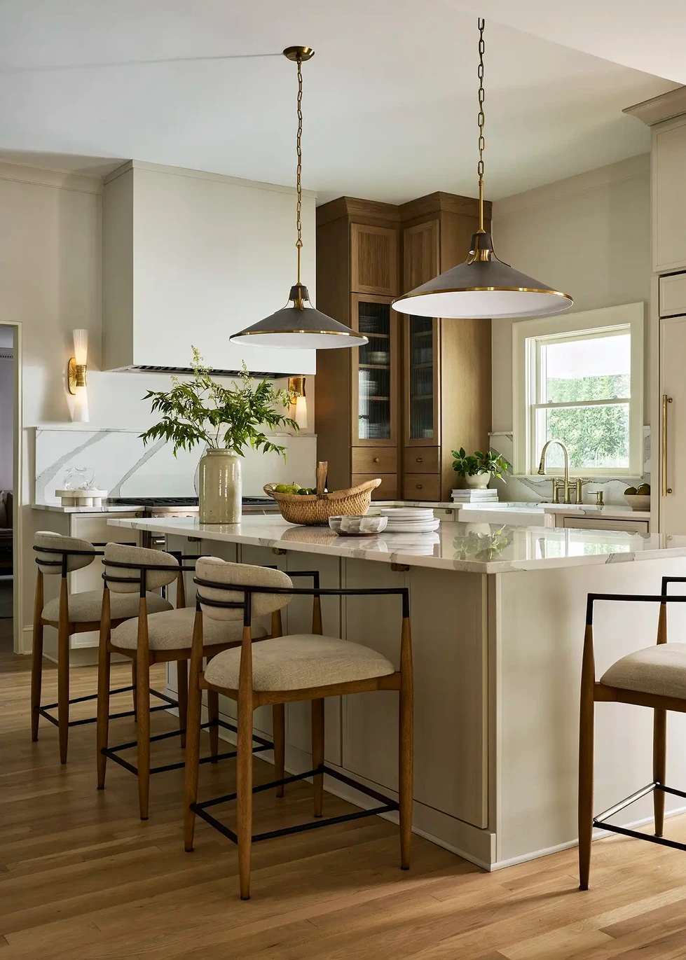 Modern transitional kitchen renovation | two-toned stained and painted cabinetry | modern hood | arched reeded wood cabinets | paneled refrigerator | paneled dishwasher | home bar with ice maker and drawer refrigerators | reeded glass cabinet doors | modern pendant lighting | quartz countertops | upholstered wood barstools