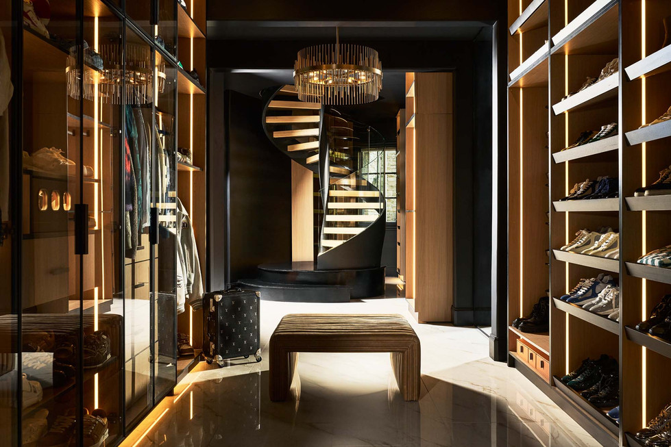 Luxury men’s walk-in closet with glass wardrobes, wood shelving, and black spiral staircase