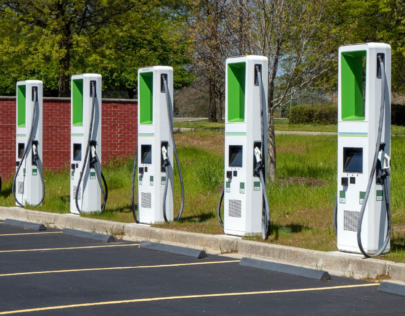 Electric car charging stations in a parking lot surrounded by greenery, illustrating the increasing availability of electric vehicle infrastructure and the potential for cost savings with electric cars