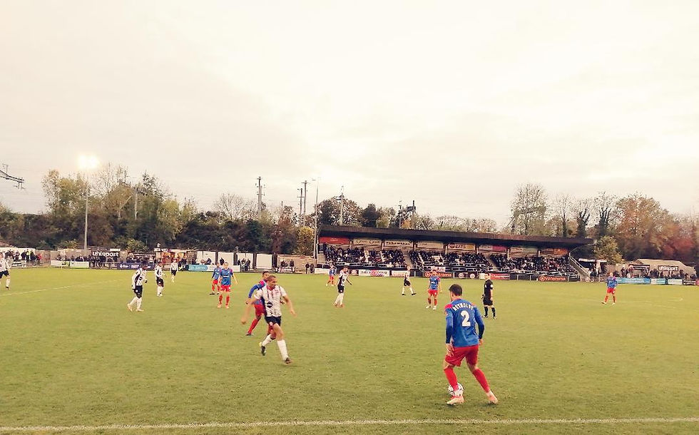 A Dagenham player, wearing a blue top and red shorts, has the ball. He is faced by a Maidenhead player with a white top and black shorts