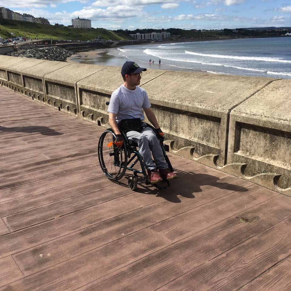 I am in my wheelchair on a sunny day, with the sea in the background