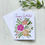 Thumbnail: White birthday greeting card with pink and yellow flowers on white wood background and green leaf.