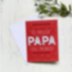 Red father's day card with 'el mejor papa del mundo' lettering on white wood background and green life. .